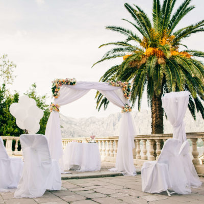 Sunset destination wedding arch on beach white chairs palm trees