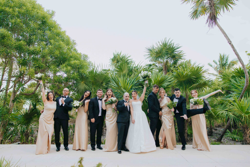 Bride, groom and wedding party cheering in champagne dresses and black tuxedos among tropical palms at UNICO 20°87° Hotel Riviera Maya